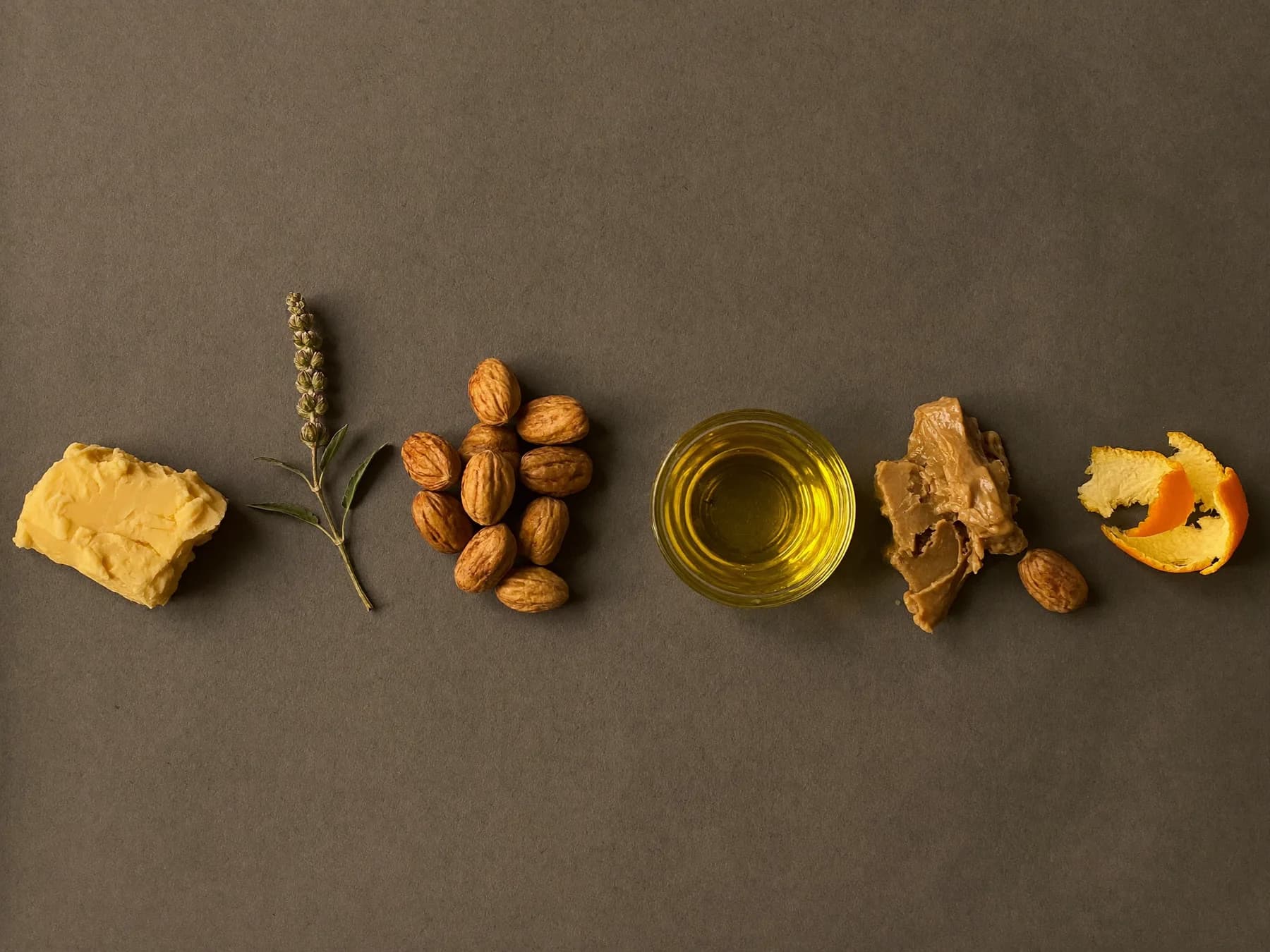 Shea nuts, cocoa butter, sunflower oil, geranium leaves and orange peel laid out in a row
