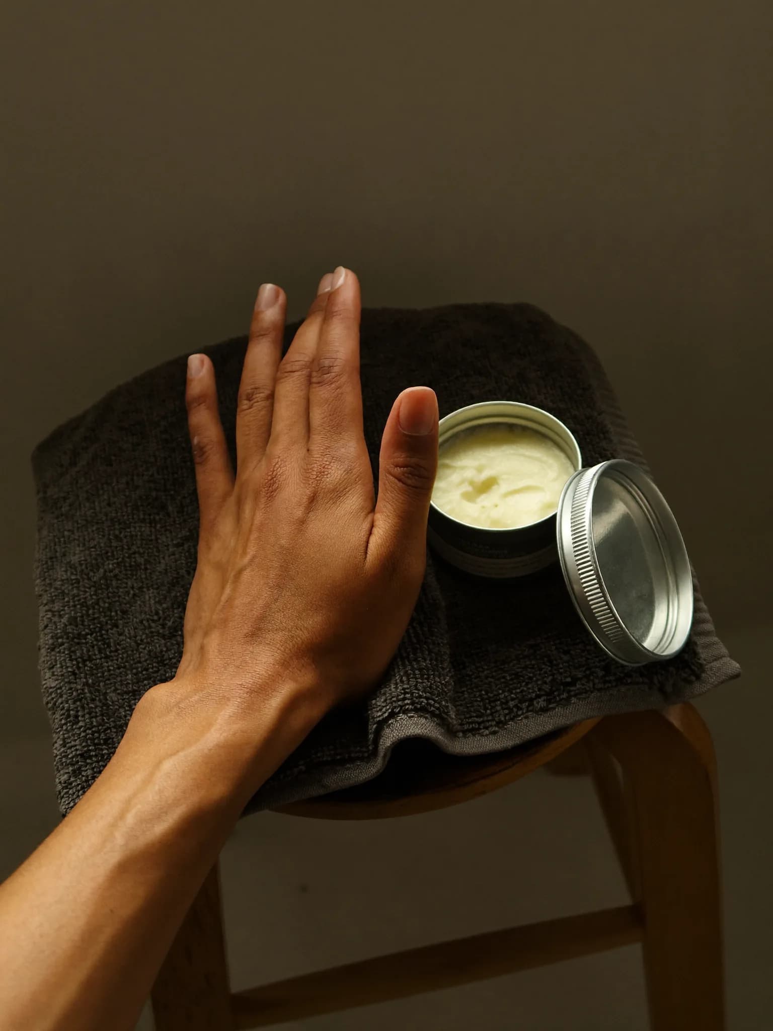 A hand resting on a folded towel next to an open tin